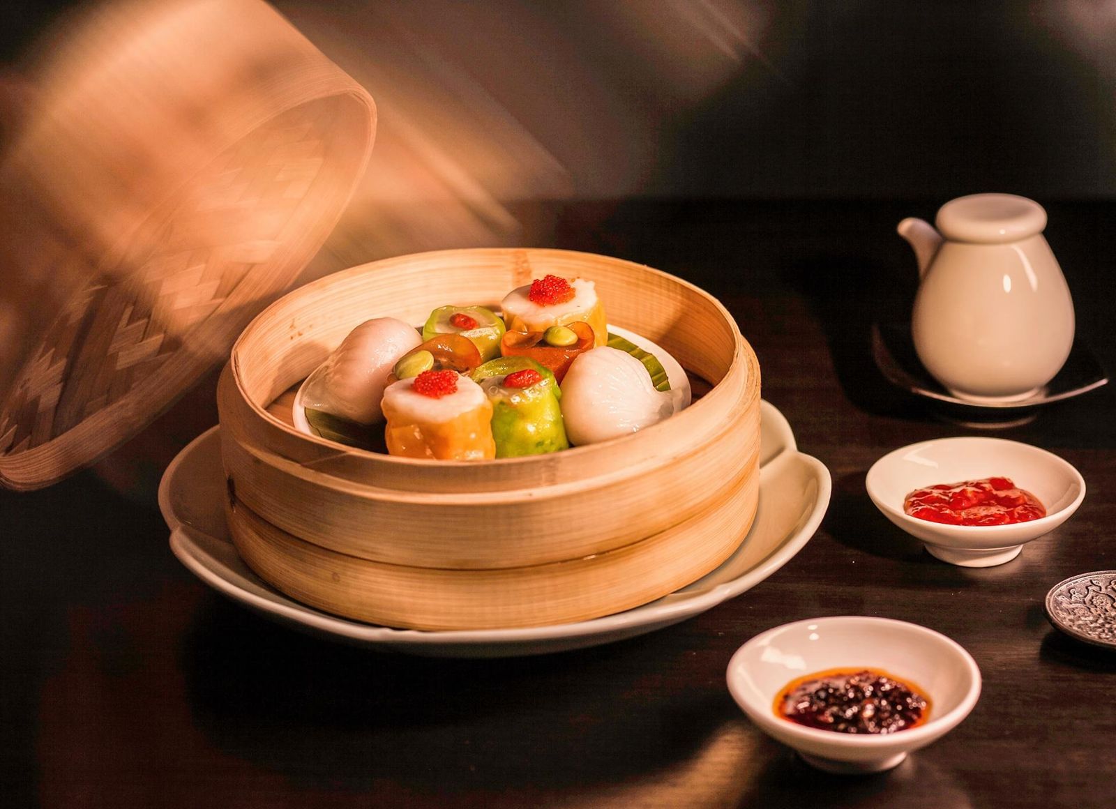 Steamed dim sum in a bamboo basket with chilli oil and tea